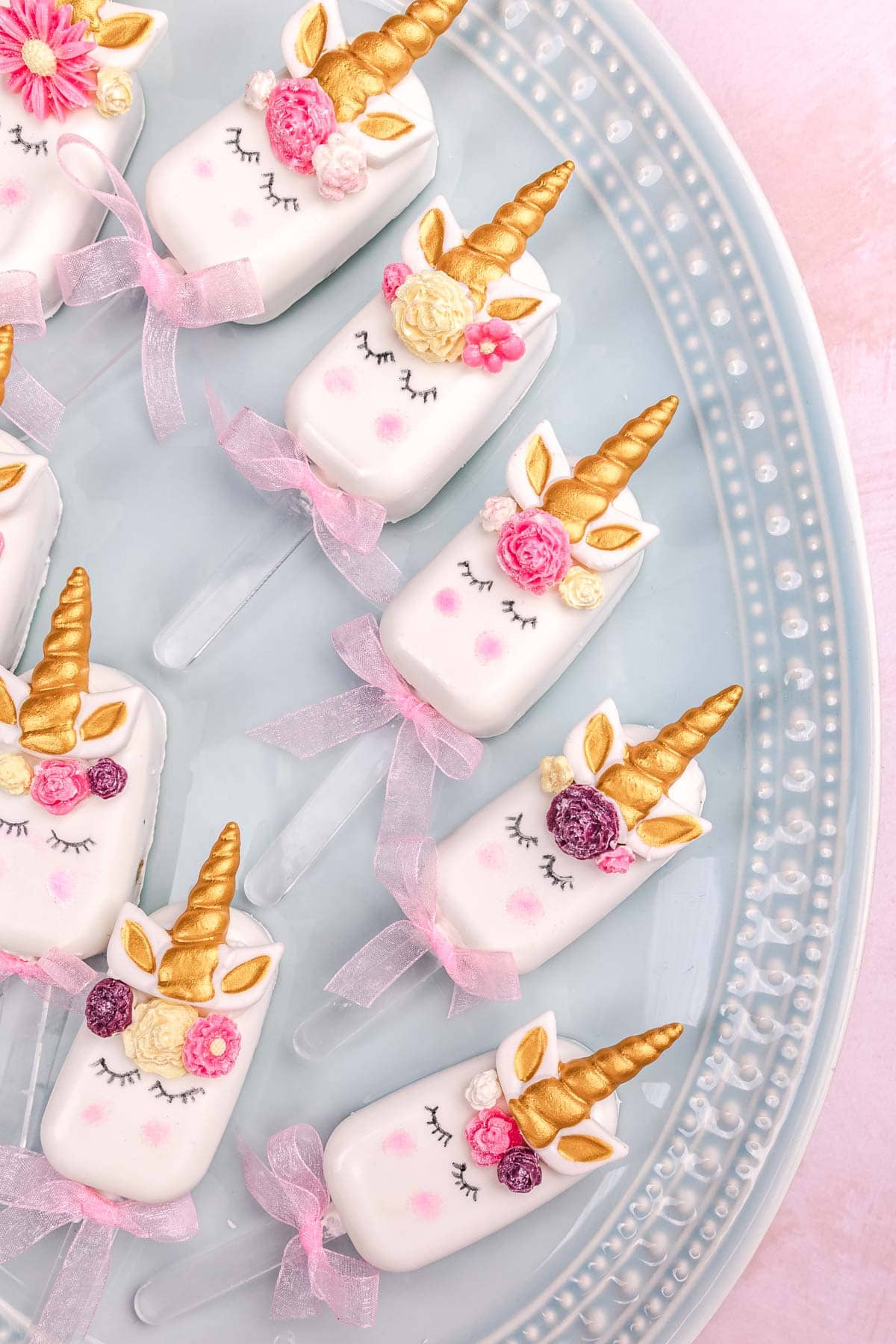 a blue platter with decorated unicorn cakesicles on top. 