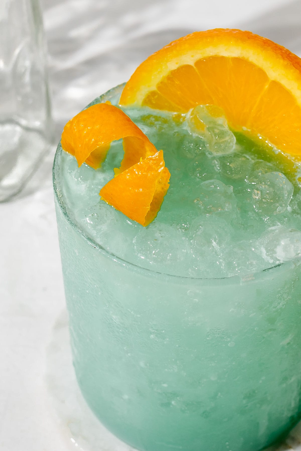an up close photo of the top of a blue drink with an orange peel on top. 