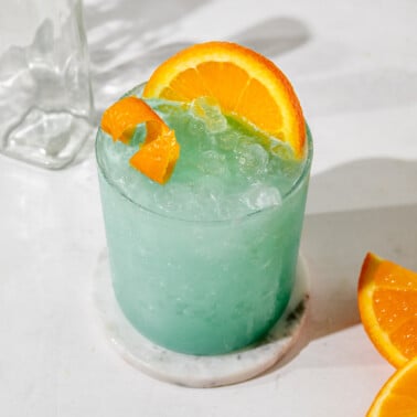 an overhead shot of a blue hawaiian mocktail in glass filled with ice and topped with and orange slice.
