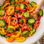 a salad bowl filled with cucumbers, bell peppers, and seasonings.