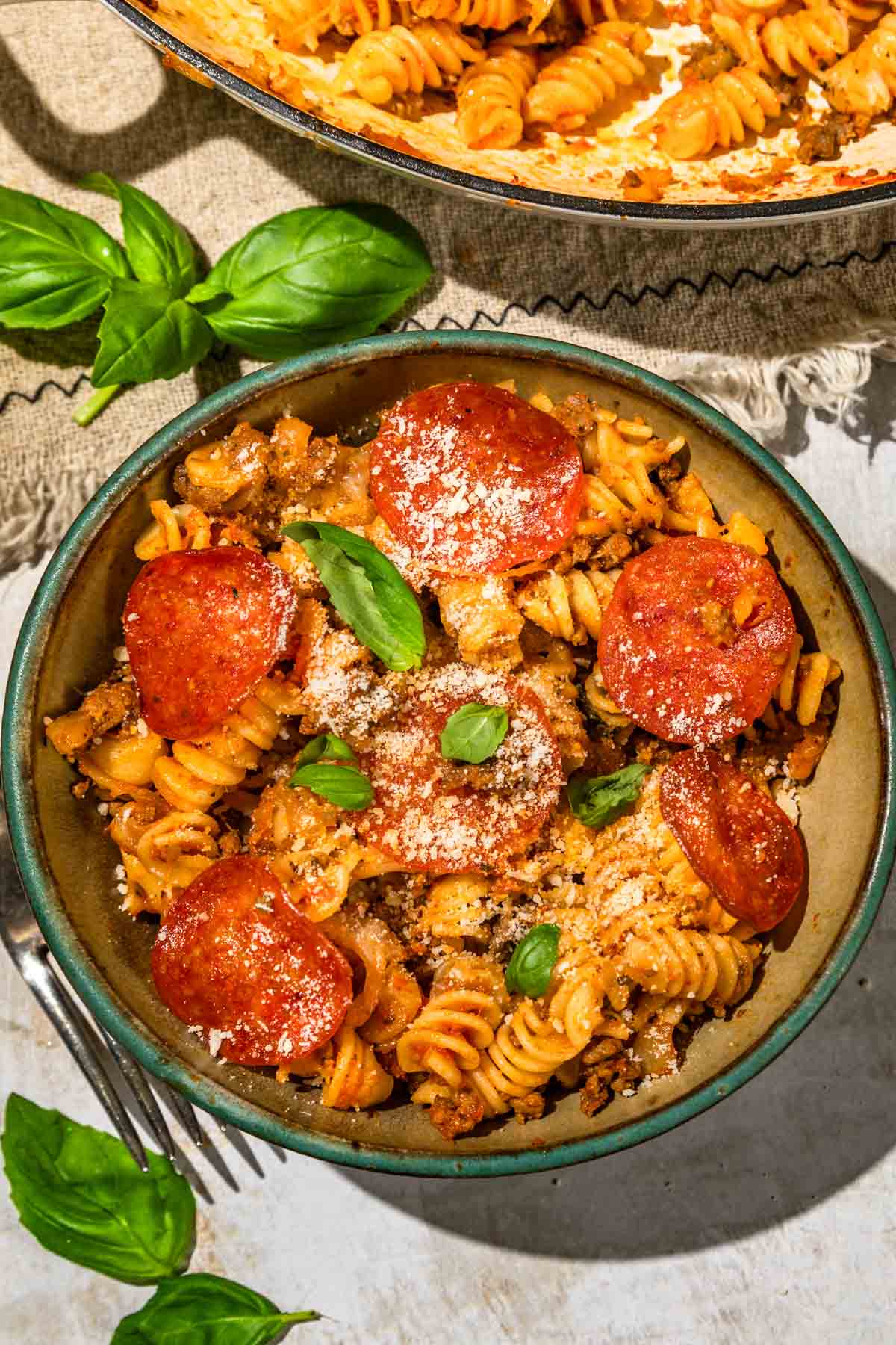 a bowl of pasta topped with pepperoni, basil, and parmesan cheese. 