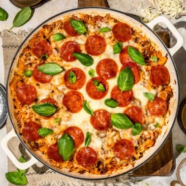 an overhead shot of a pizza pasta bake topped with pepperoni and basil