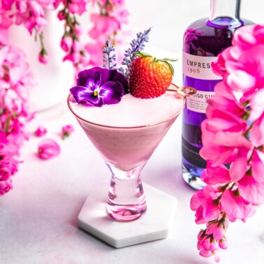 a strawberry gin cocktail in a glass topped with a fresh strawberry, lavender, and purple flower.