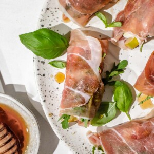 a plate with prosciutto wrapped mozzarella roll ups garnished with fresh basil.