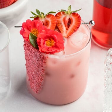 a glass filled with ice and a pink drink recipe and garnished with strawberries