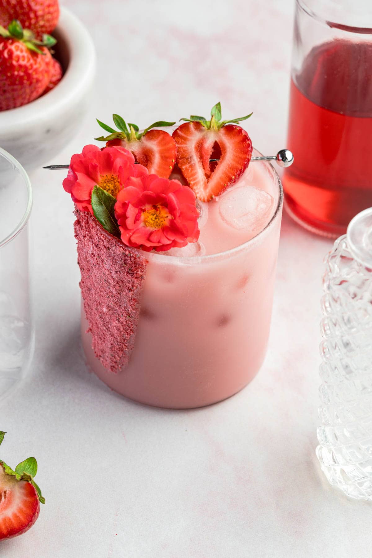 a glass filled with ice and a pink drink recipe and garnished with strawberries 
