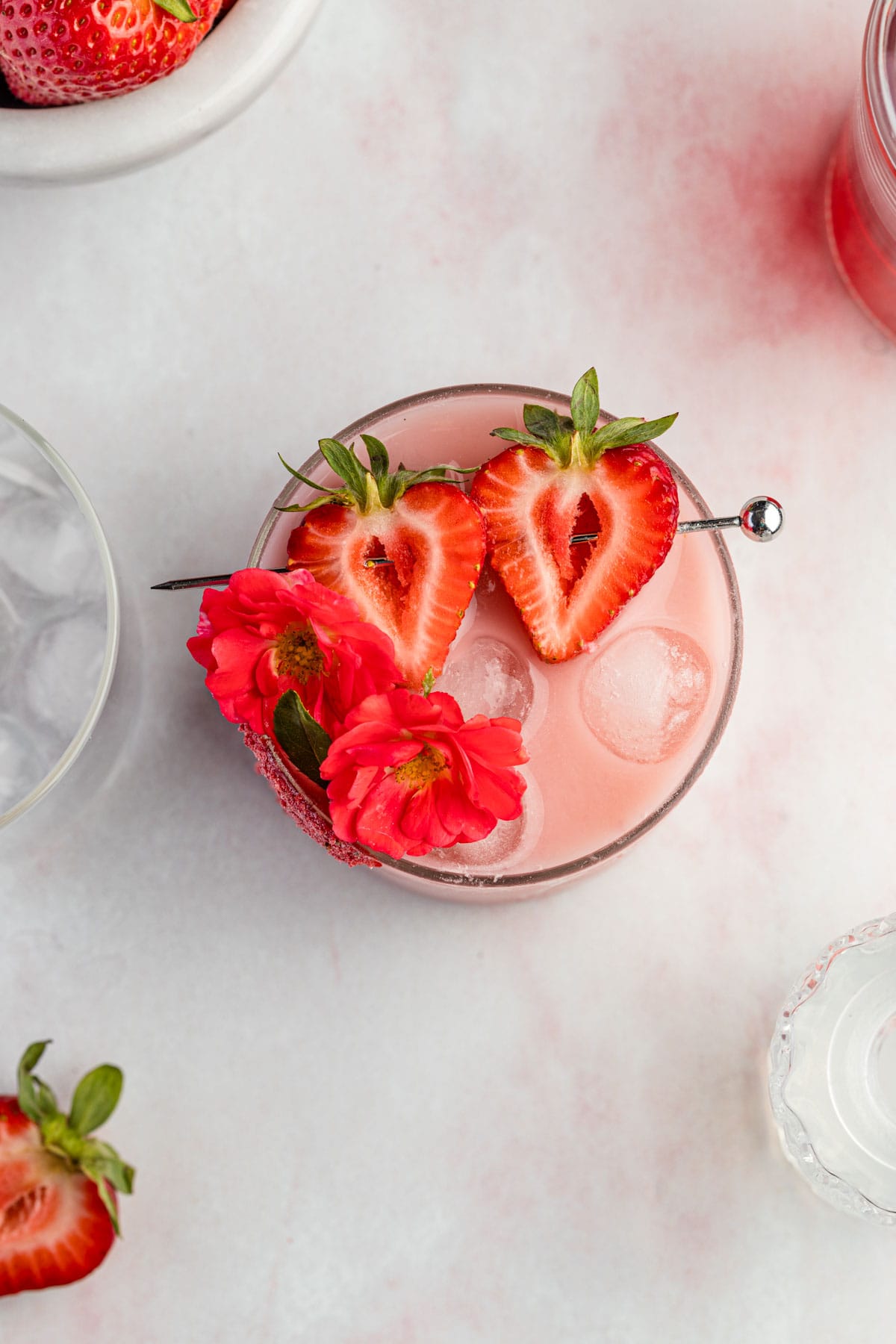 an overhead shot of a pink drink filled with ice and topped with strawberries and flowers. 