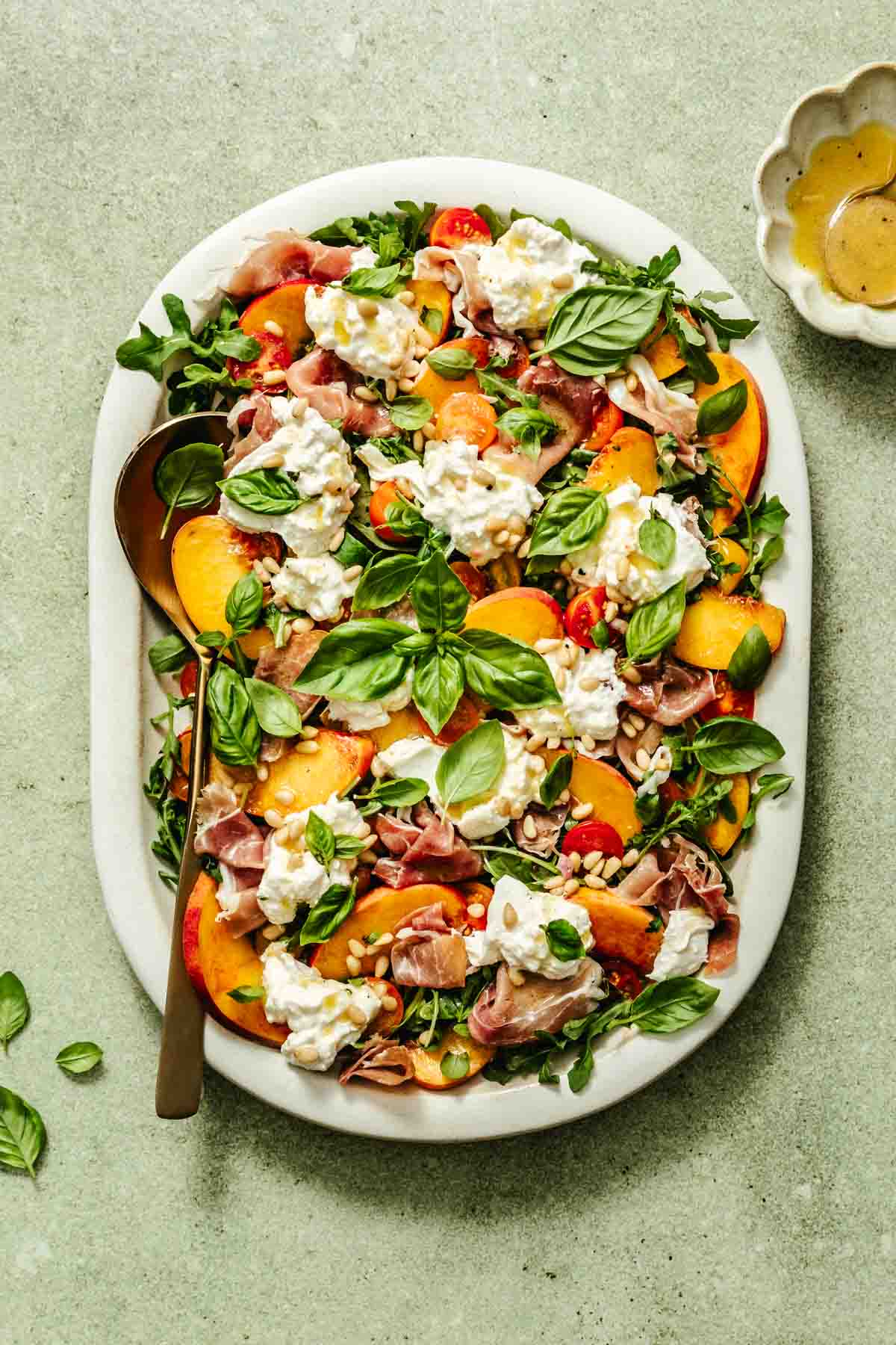 an overhead shot of a peach burrata salad on a white serving platter with a gold serving spoon 