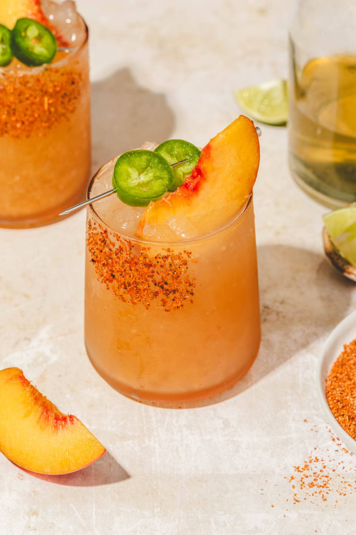 a spicy peach margarita mocktail in a glass topped with sliced jalapenos and peaches. 