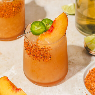 a spicy peach margarita mocktail in a glass topped with sliced jalapenos and peaches.