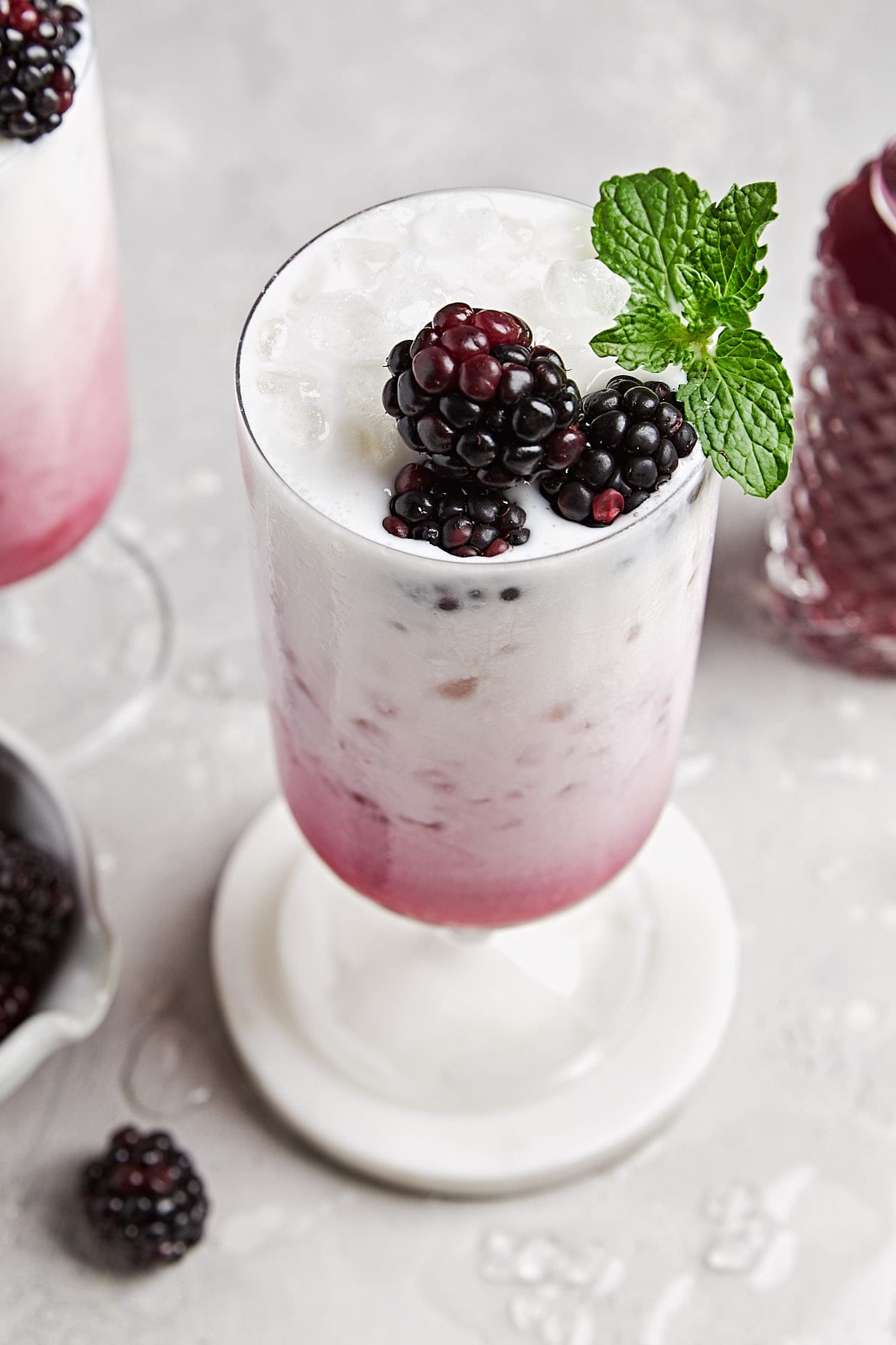 an overhead shot of a an Italian soda recipe in a tall glass topped with three blackberries and mint sprig