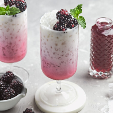 a glass filled with blackberry italian soda recipe with fresh berries and mint on top.