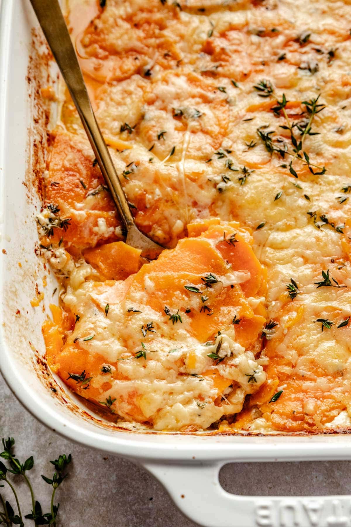Sweet potato au gratin in a large white baking dish with a serving spoon scooping out a corner piece.