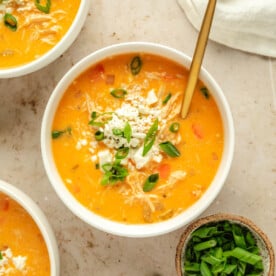 an overhead shot of buffalo chicken soup in a white bowl with a gold spoon