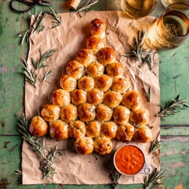 dough balls shaped into pull apart Christmas tree bread next to a small bowl of marinara sauce.