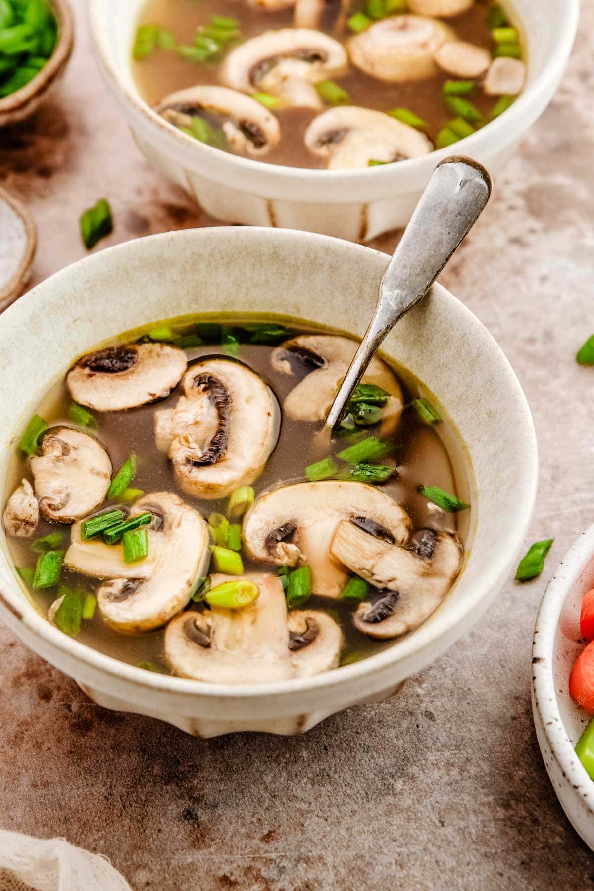 A bowl of clear broth with mushrooms and green onions