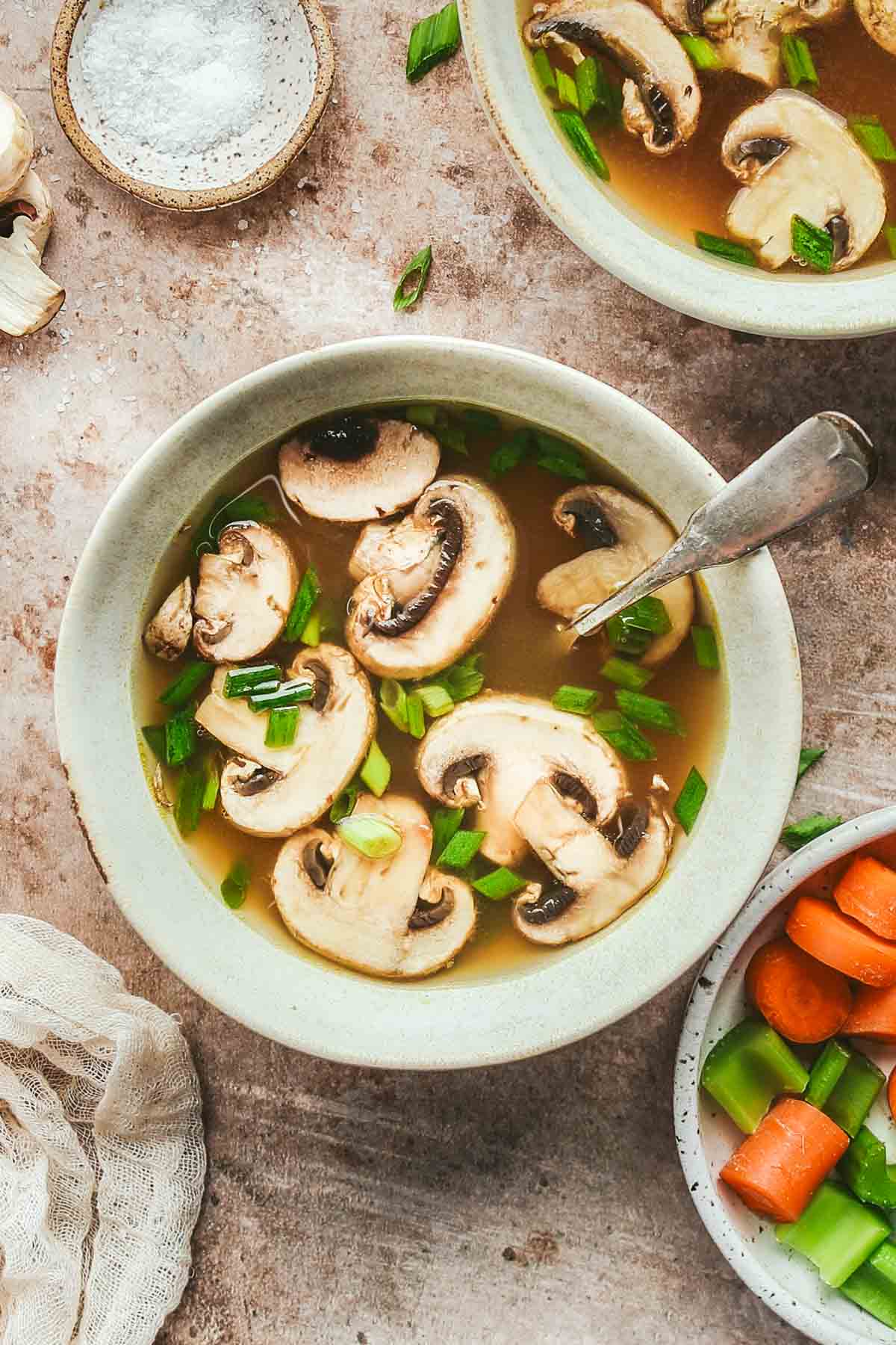 a overhead shot of a bowl of clear onion soup garnished with mushrooms and green onions