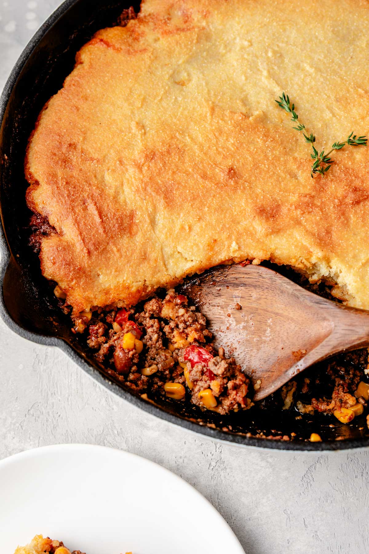 a wooden spoon resting in a cast iron pan filled with cowboy cornbread casserole