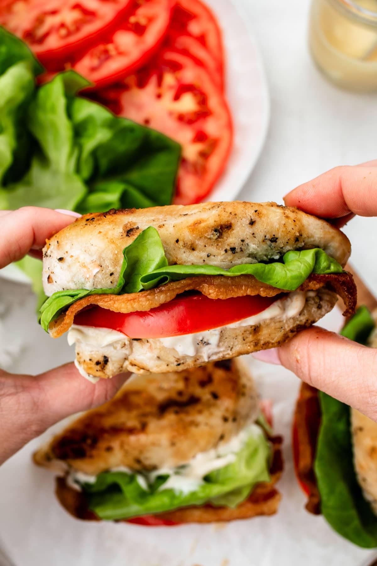 a hand holding one keto stuffed chicken breast with bacon, lettuce, tomato, and mayo 