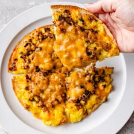 a hand holding a slice of this breakfast pizza recipe