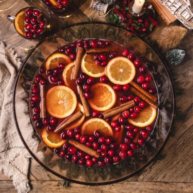 non-alcoholic christmas punch in a large bowl topped with orange slices, cranberries, and cinnamon sticks