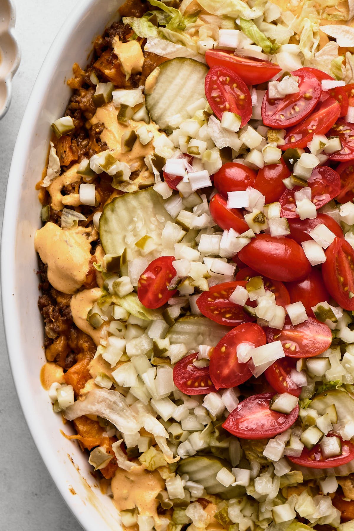 an overhead shot of a big mac casserole topped with tomatoes, onions, and pickles