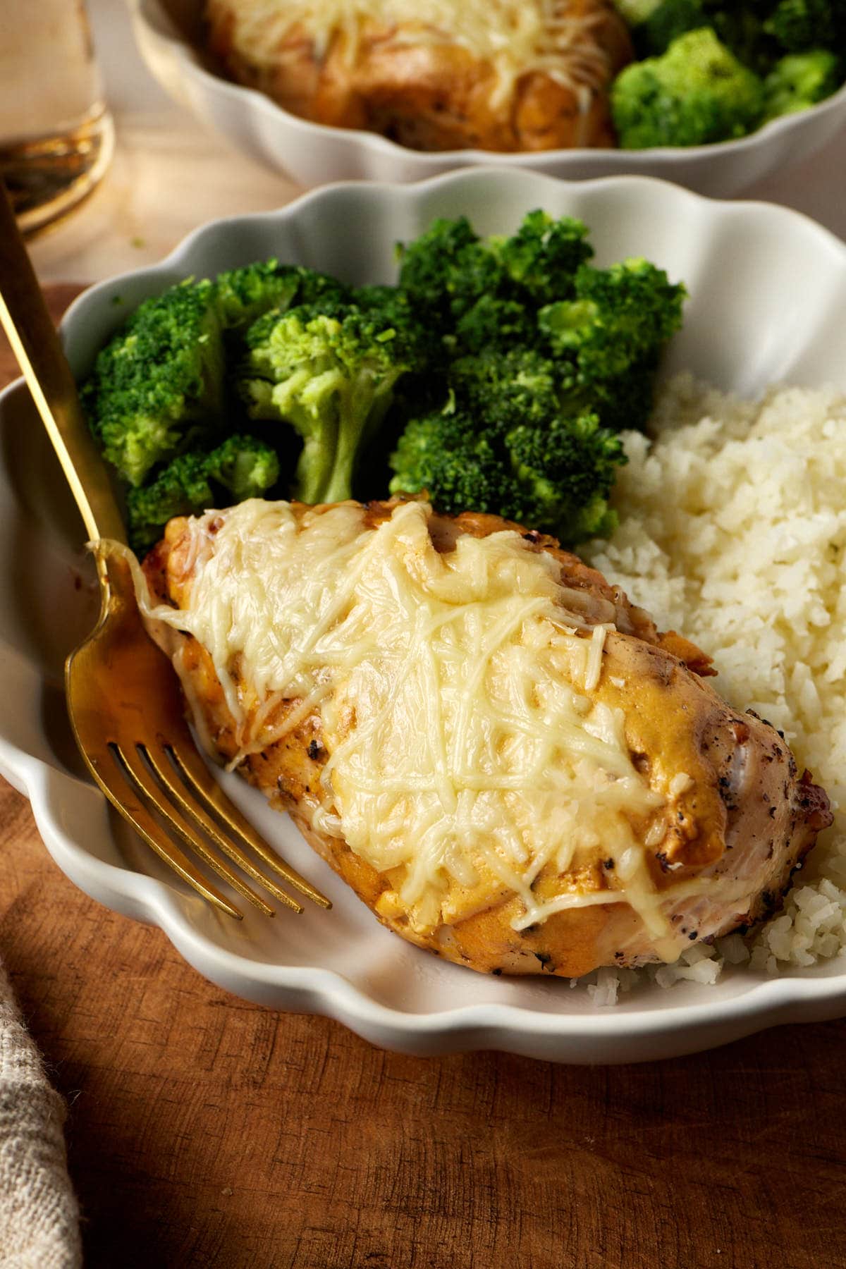 cast iron chicken breast smothered with cheese and cottage cheese sauce on a plate next to broccoli and rice