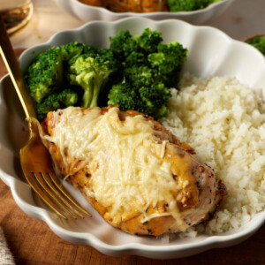 cast iron chicken breast smothered with cheese and cottage cheese sauce on a plate next to broccoli and rice
