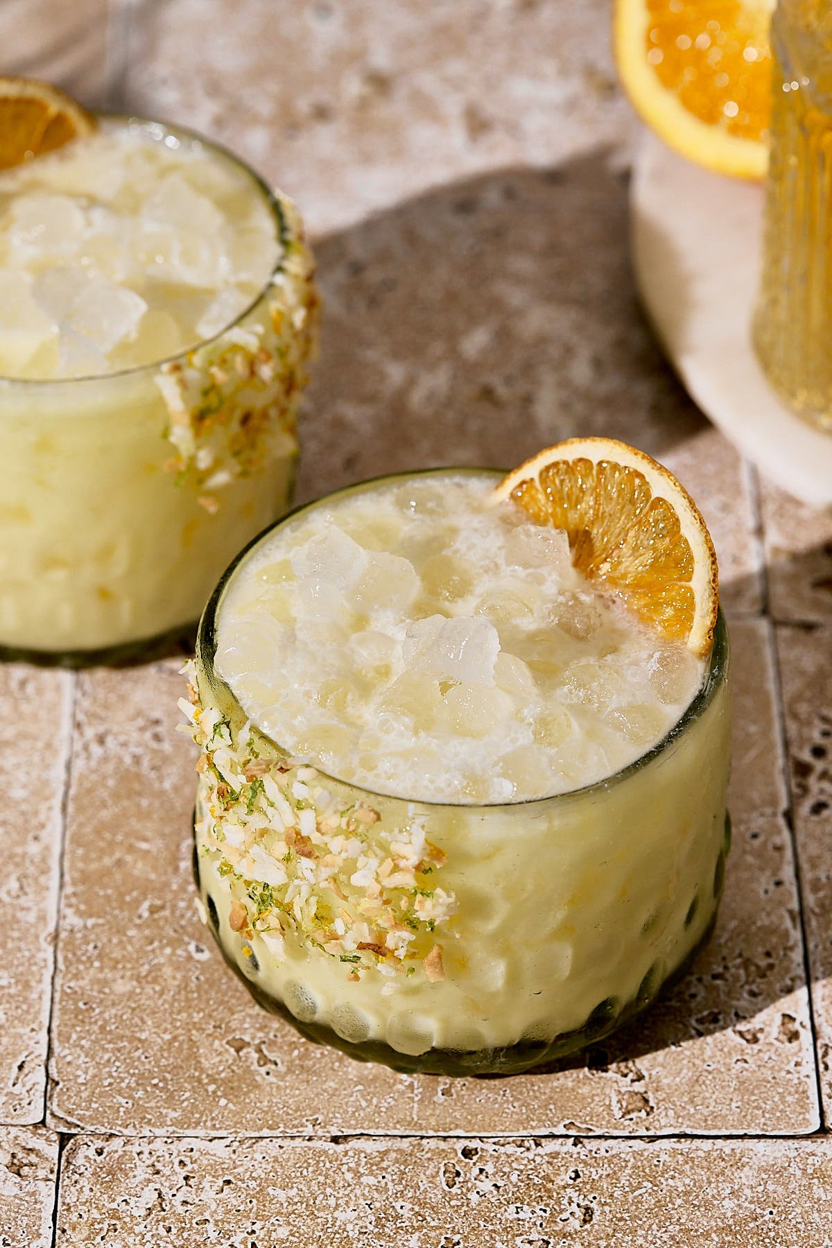 two glasses filled with creamsicle margarita drink and topped with an orange slice. 
