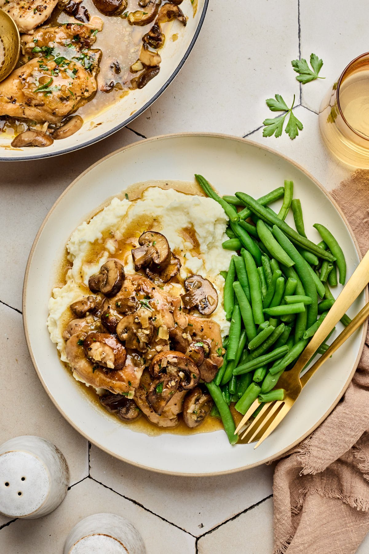 a bowl with mashed potatoes covered with the chicken thighs and wine sauce with a side of green beans