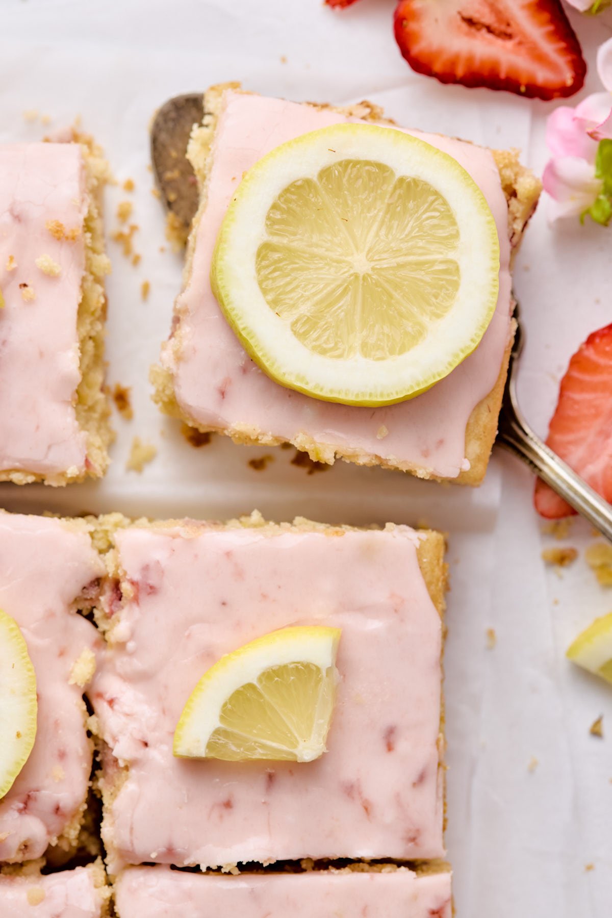 an overhead shot of strawberry lemon blondies topped with pink icing and a fresh lemon wheel 