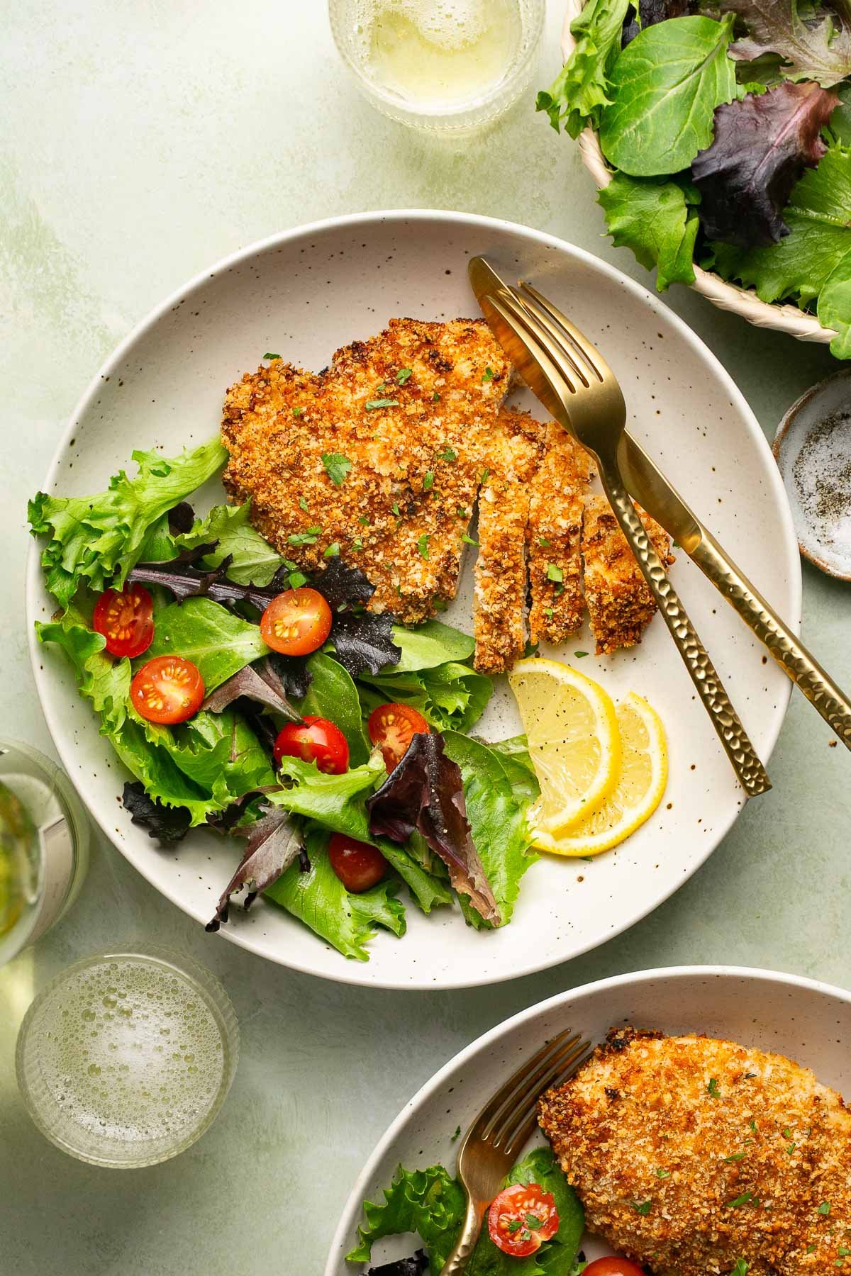 an air fryer chicken cutlet on a plate with a side salad and two lemon slices