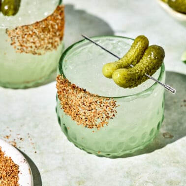 a pickle margarita in a short glass with two pickles resting on top