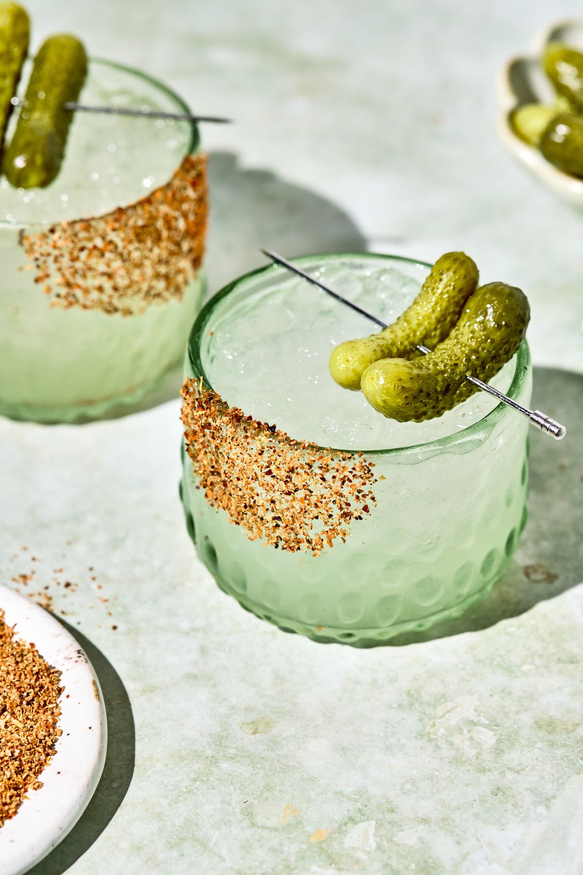 a pickle margarita in a short glass with two pickles resting on top