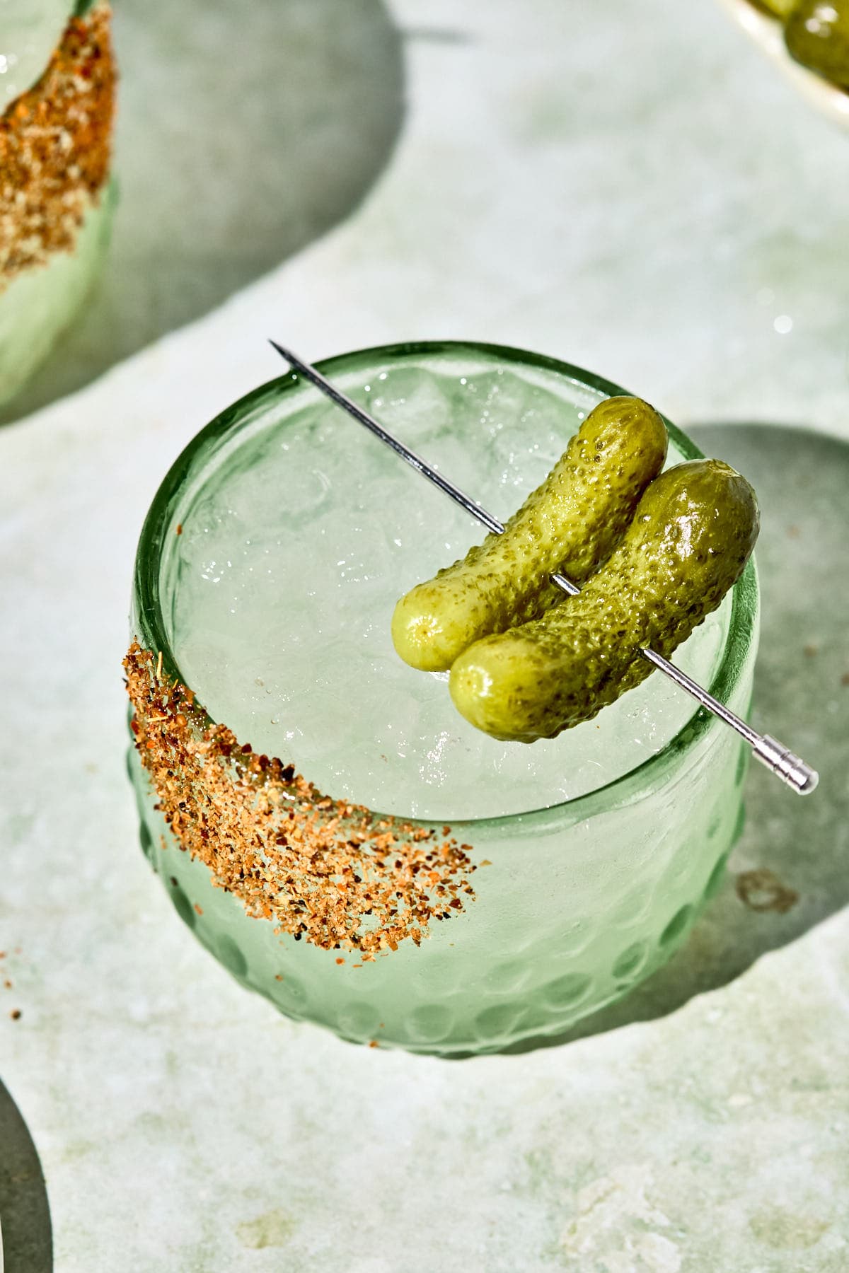 an overhead shot of a mocktail in a glass with a tajin rim and pickles on top