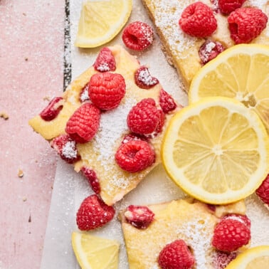 an up close photos of dessert bars topped with lemons and raspberries