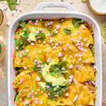 chicken tortillas casserole in a white baking dish topped with cilantro, avocado and red onion