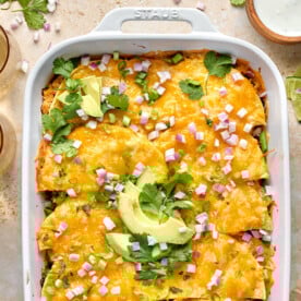 chicken tortillas casserole in a white baking dish topped with cilantro, avocado and red onion