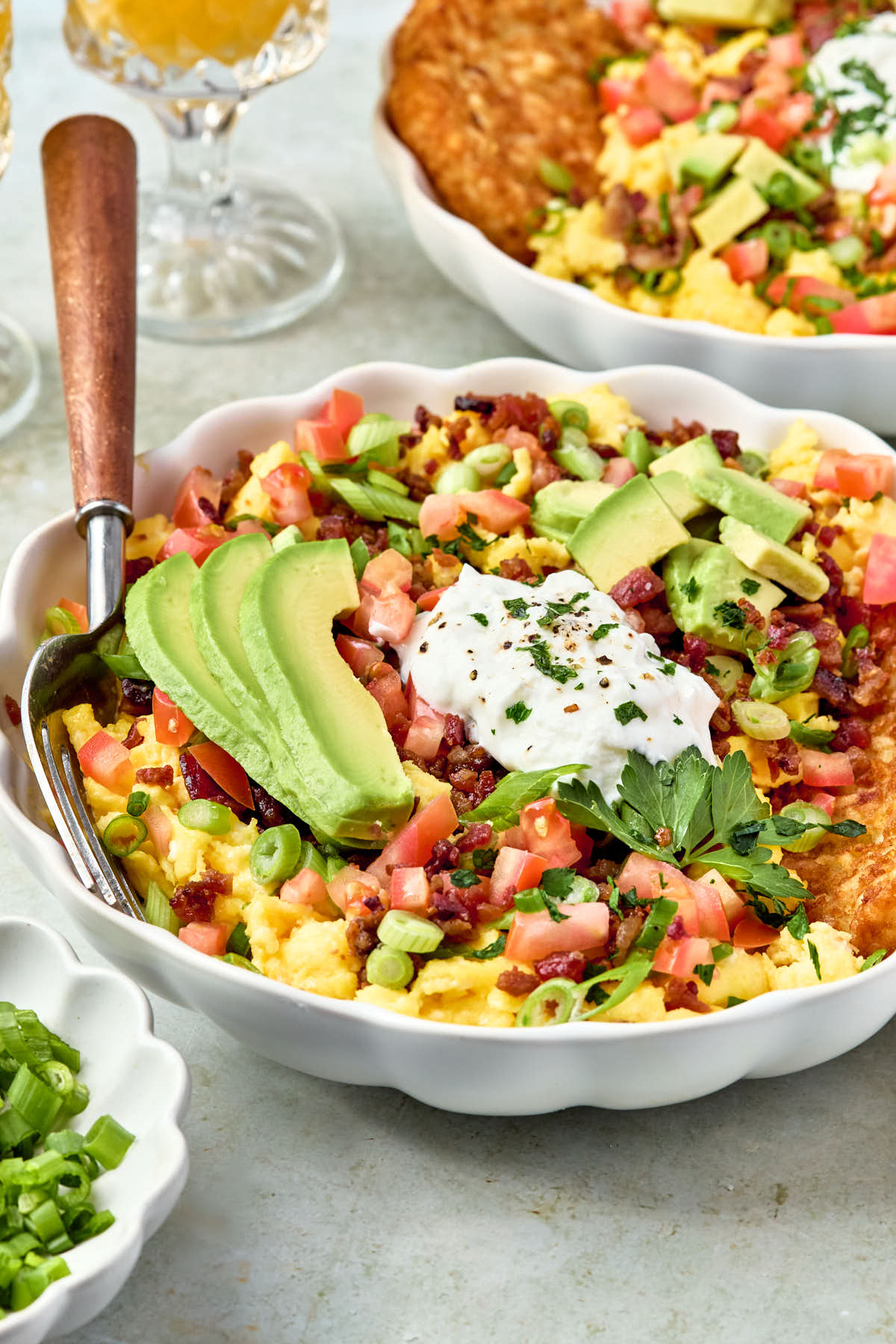 a side view of a white bowl filled with eggs, bacon, tomatoes, onions, avocado, and greek yogurt