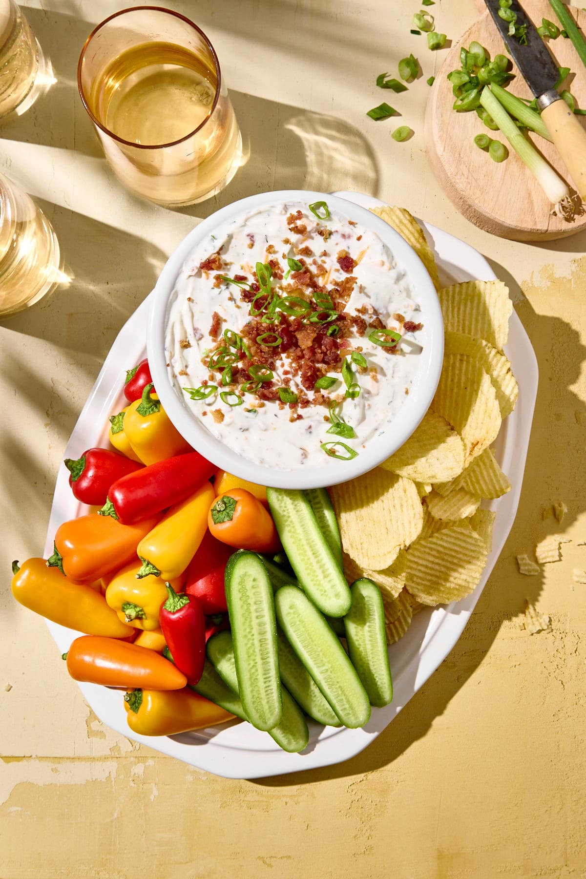 An overhead shot of a platter with chips, peppers, cucumbers and crack dip