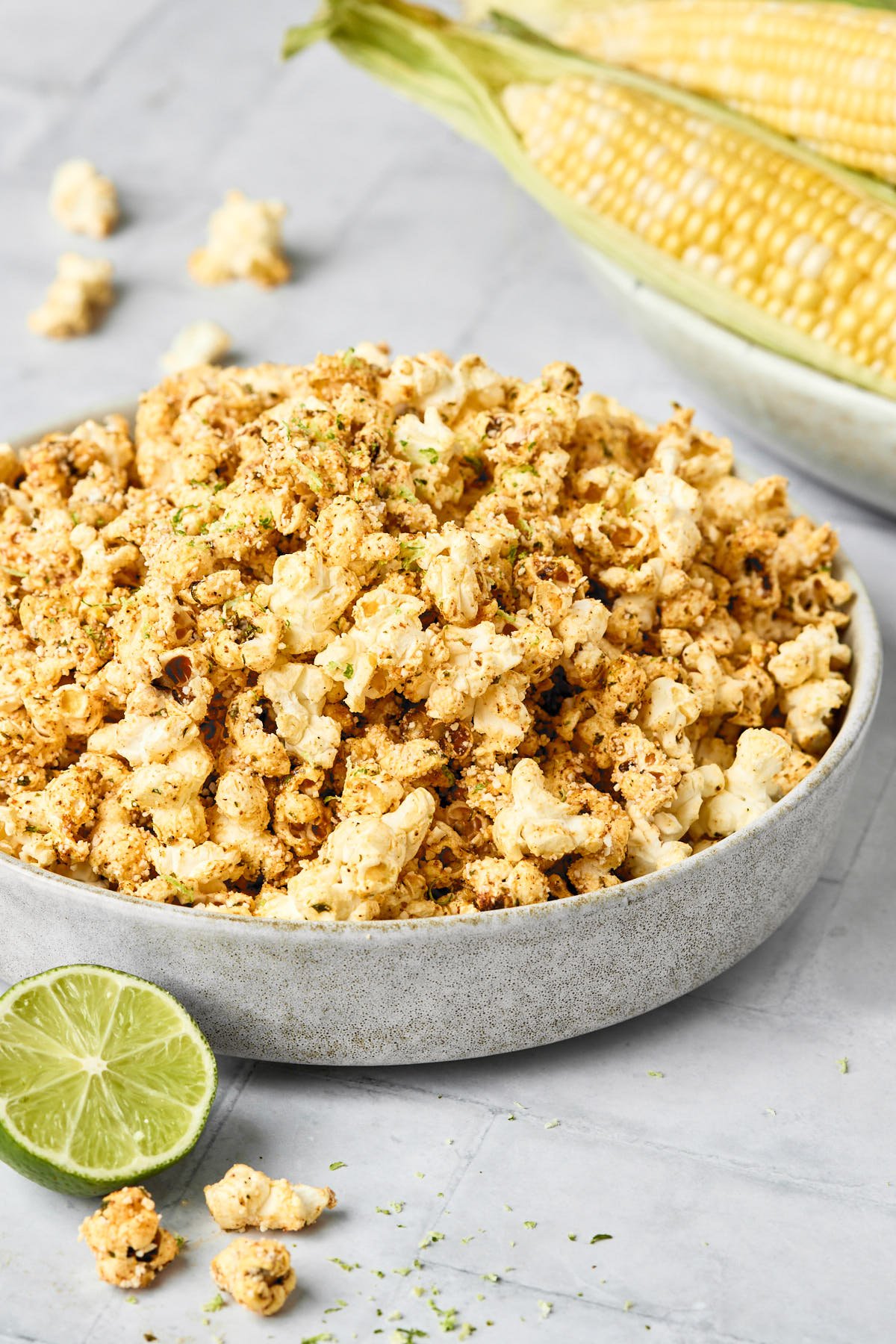 a grey bowl filled with street corn popcorn with a lime sitting beside the bowl and corn in the background
