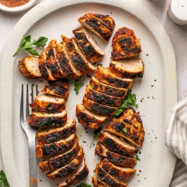 a platter of sliced chicken topped with fresh parsley