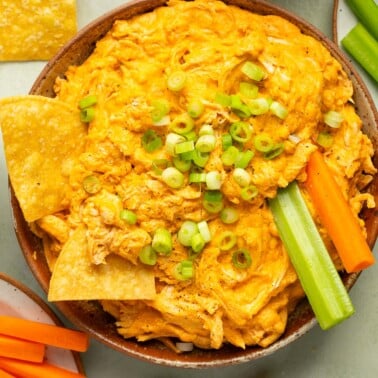 crockpot buffalo chicken dip in a bowl with tortilla chips, celery, and carrots