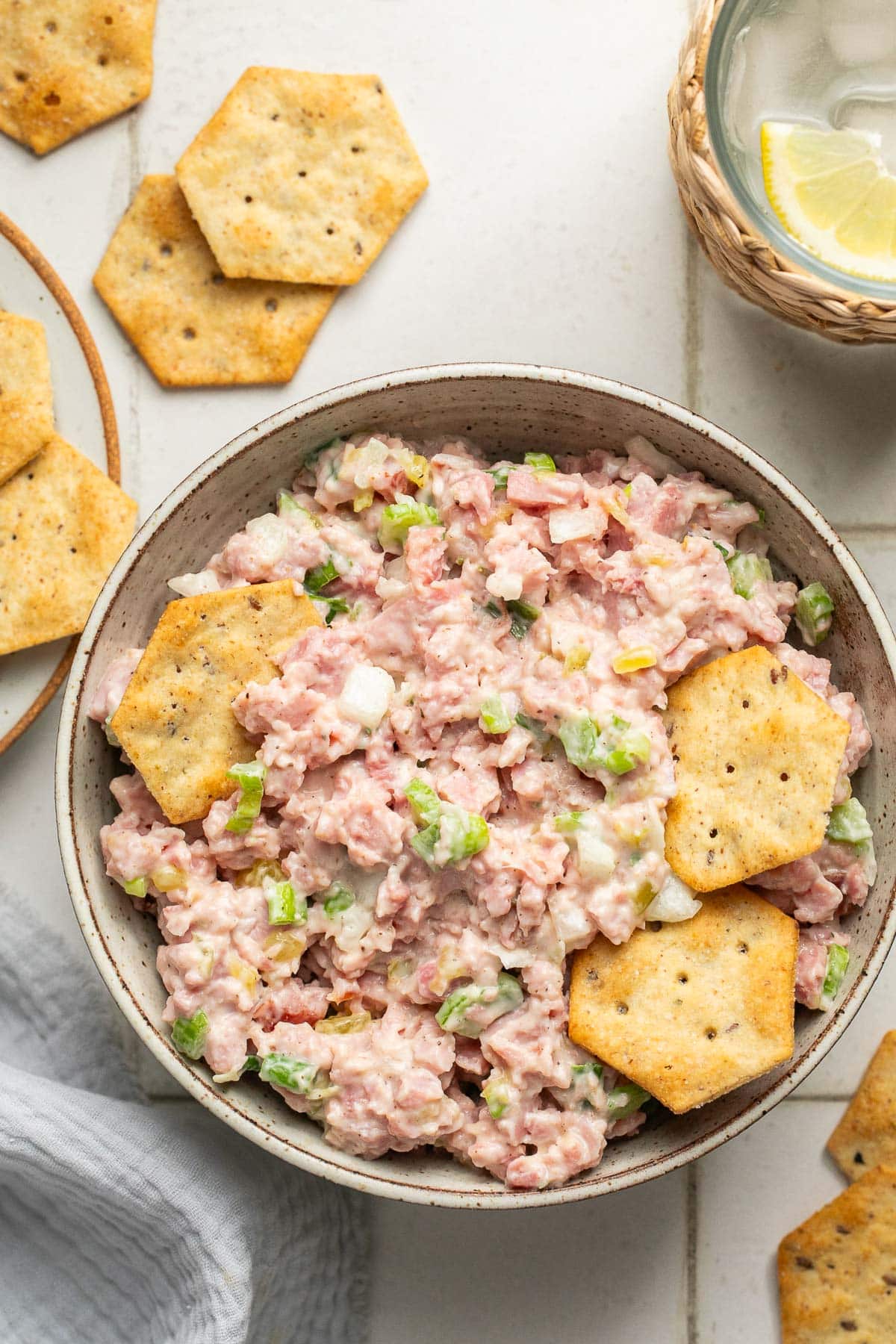 a bowl filled with chopped ham, veggies, and creamy dressing with crackers resting on top