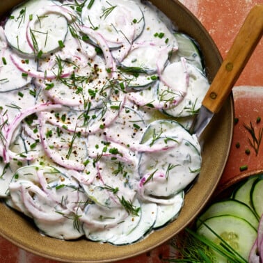 an overhead photo of greek yogurt cucumber salad in a brown bowl with a spoon