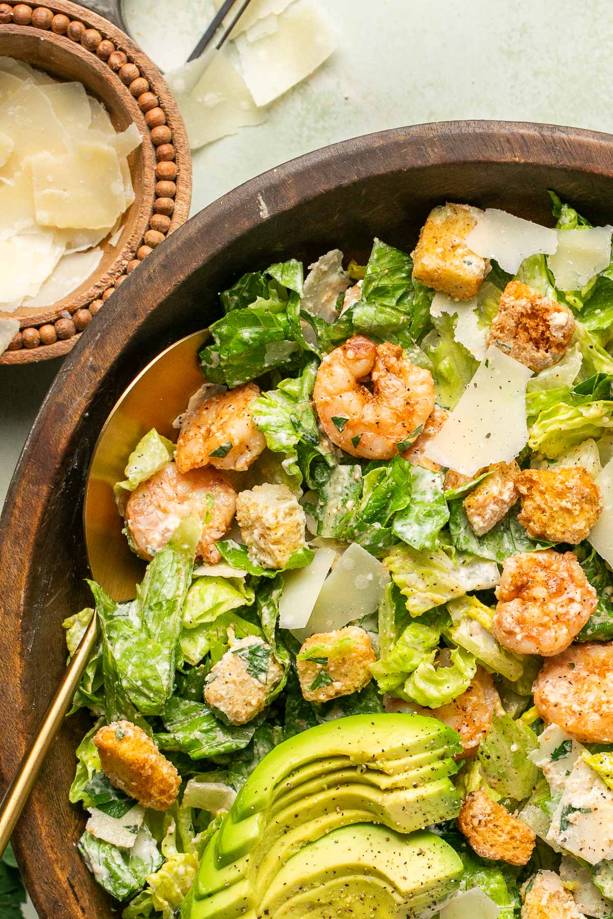 a close up of shrimp caesar salad in a salad bowl with gold tongs