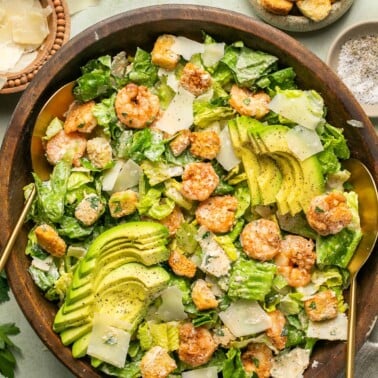 an overhead shot of a shrimp caesar salad tossed in a wooden salad bowl