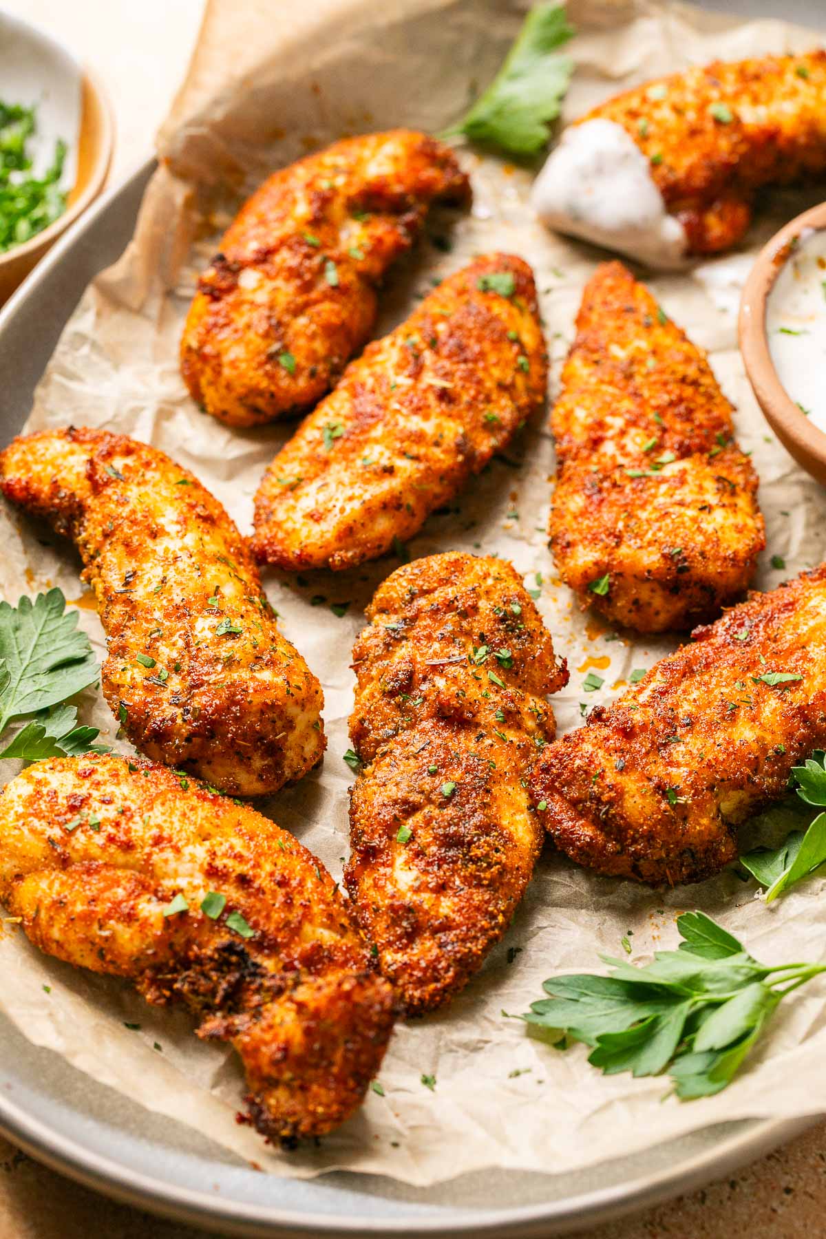 an up close shot of chicken tenders on a platter with fresh parsley to garnish 