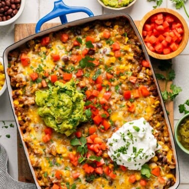 an overhead shot of taco casserole topped with cilantro, sour cream, and guacamole