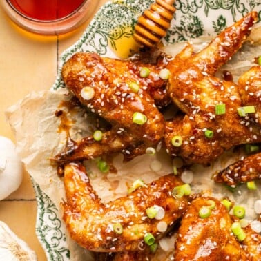 honey baked wings on a serving platter topped with sesame seeds and chopped green onions